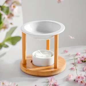 Brûle-parfum avec base en bois rond, deux colonnes verticales en bois et coupelle blanche en céramique, avec bougie chauffe-plat placée en dessous, décor floral en arrière-plan.