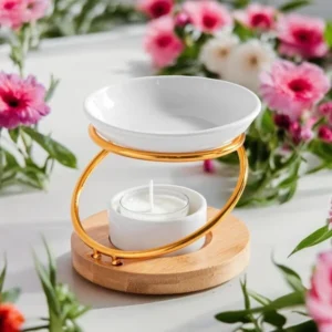 Brûle-parfum Hula en céramique blanche avec support doré et base en bois, entouré de fleurs roses.