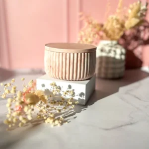 Boîte décorative en Jesmonite marbrée rose, couvercle fermé, surface rainurée verticalement, création artisanale Lez'arômes de Sandrine, posée sur un socle blanc avec fond rose et fleurs séchées.