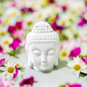 Brûle-parfum en forme de tête de Bouddha blanche entouré de fleurs colorées.