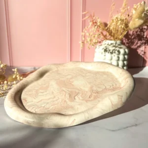 Plateau décoratif en Jesmonite marbrée beige rosé, forme organique irrégulière avec rebords arrondis, création artisanale Lez'arômes de Sandrine, sur fond rose avec fleurs séchées.