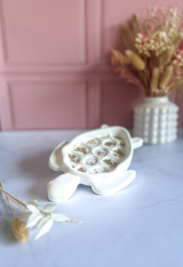 lateau décoratif en Jesmonite en forme de tortue, avec incrustations feuille d'or, posé sur une table blanche devant un mur rose.